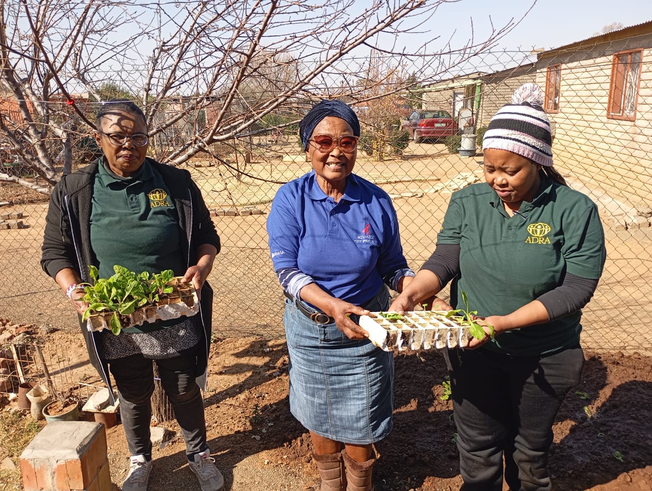 ADRA staff and a community partner holding trays of seedlings ready for planting