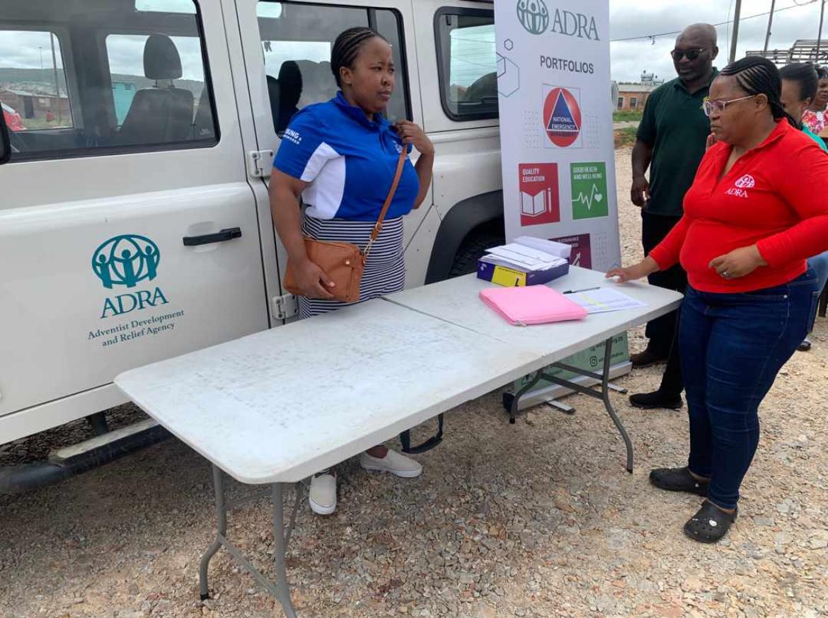 ADRA team assisting a community member at an outdoor table beside a branded ADRA vehicle