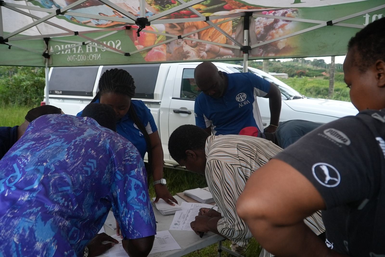 Community members and ADRA staff gathered around a registration table under a branded gazebo